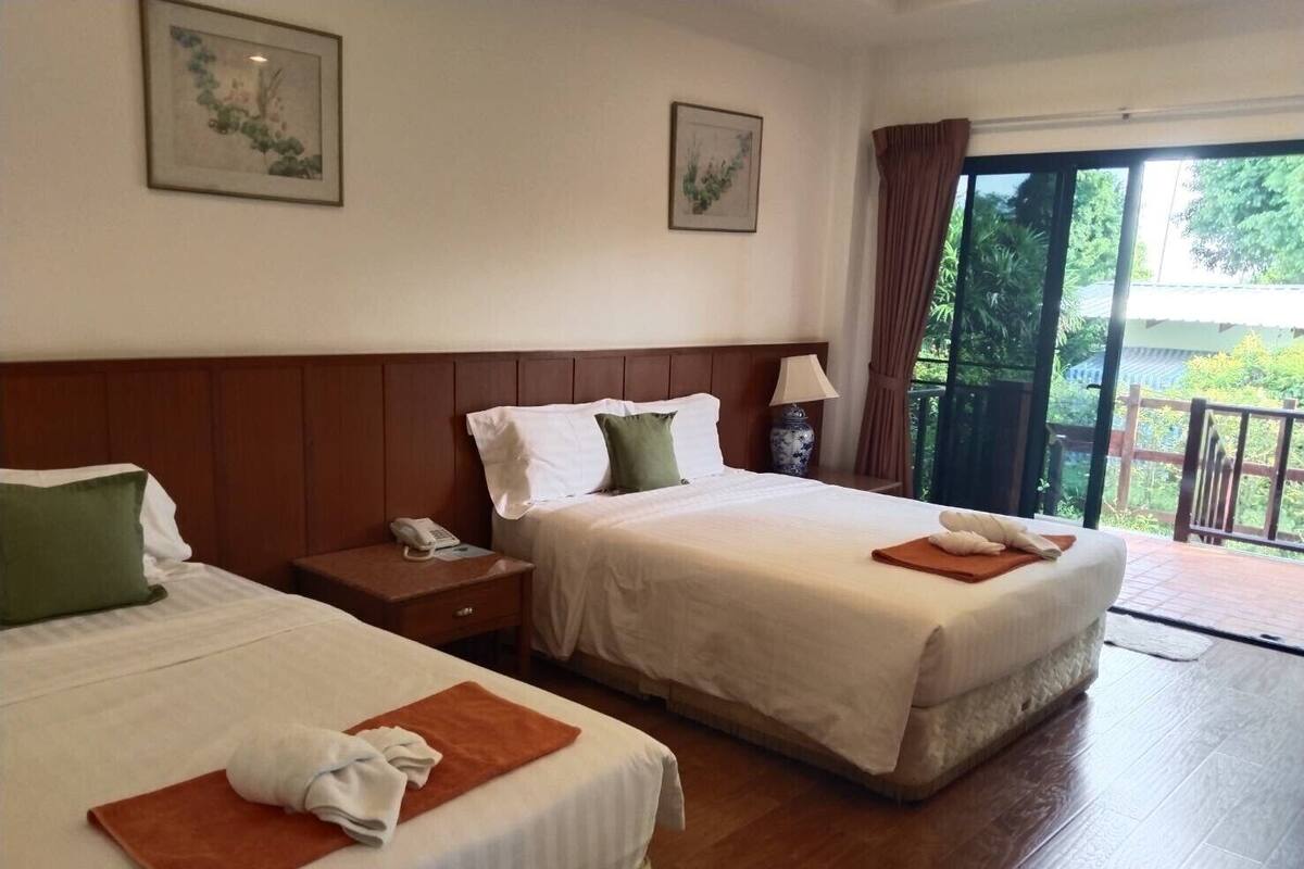 A hotel room with two beds, a nightstand with a phone, a lamp, and a view of the outdoors.
