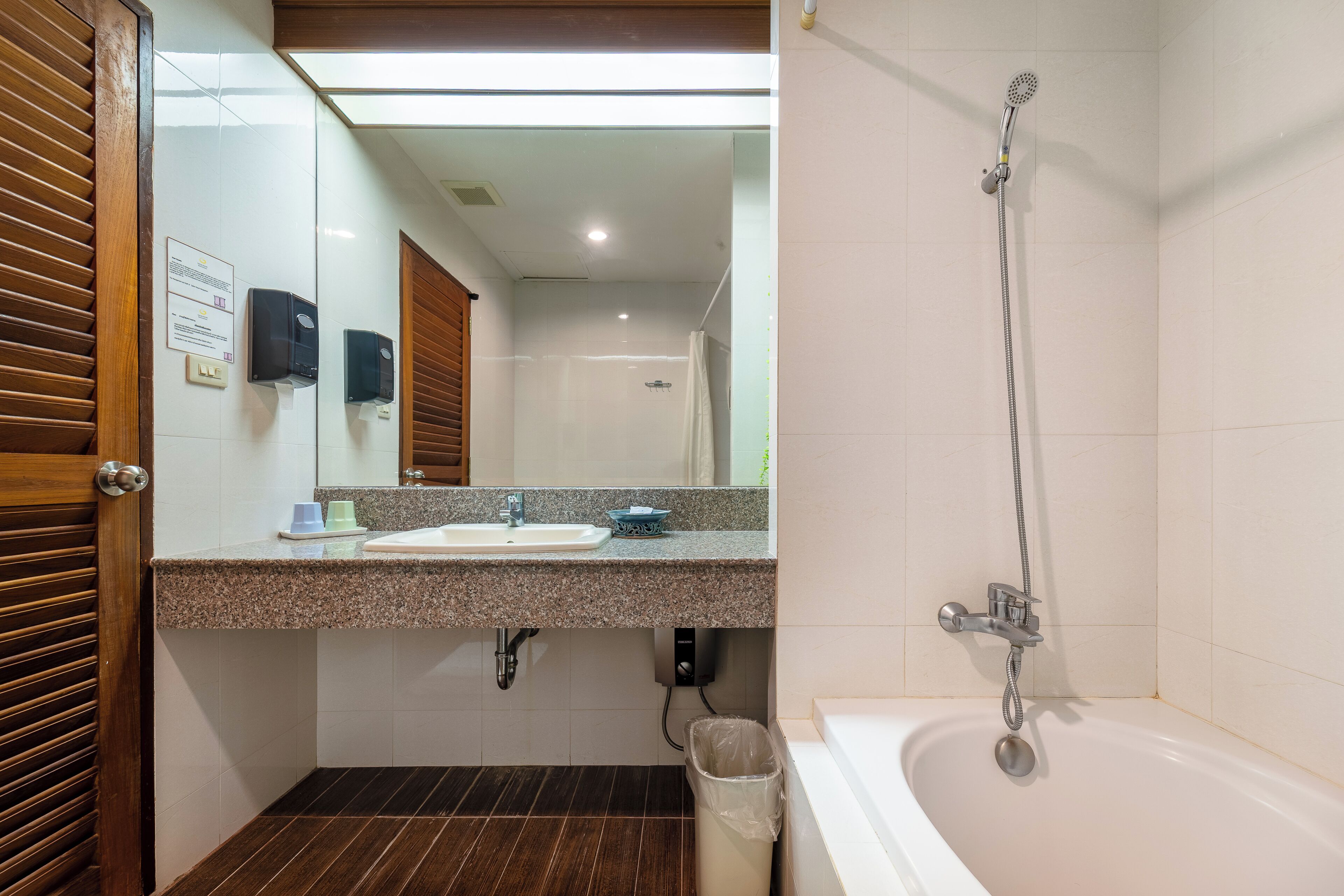 A bathroom with a sink, mirror, shower, and a trash bin.