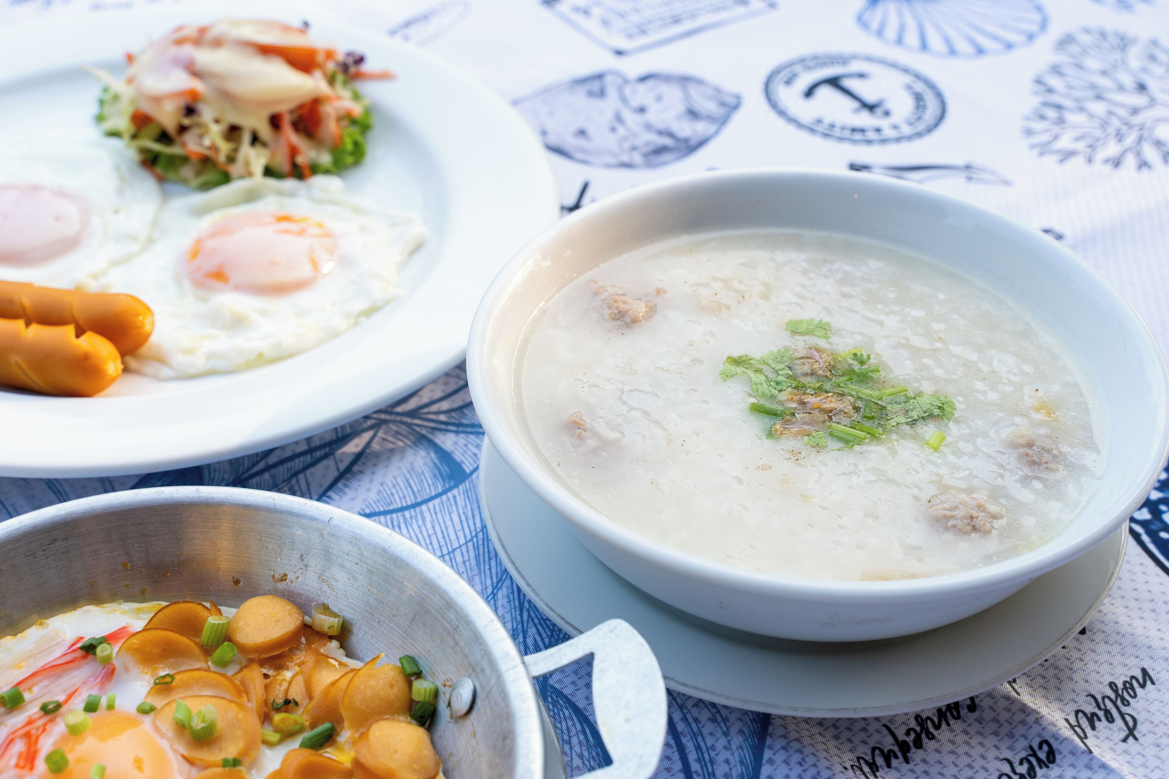 A table with a bowl of soup, a plate with eggs and vegetables, and a bowl with sliced vegetables.