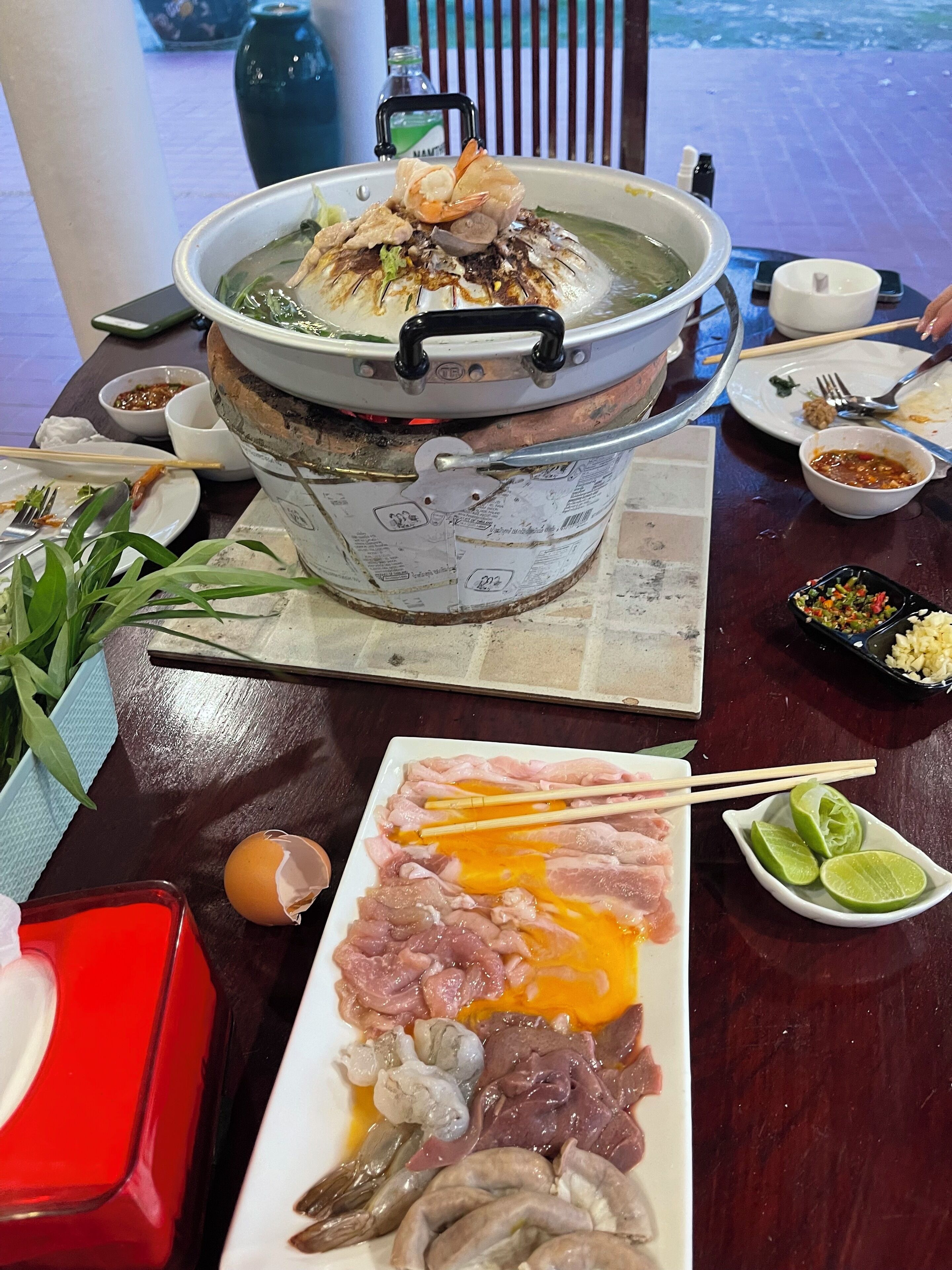 Una mesa de comedor con una olla grande de sopa, varios platos y condimentos.