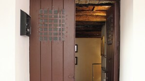 Puerta marrón que da a una habitación con una cama, una silla y una lámpara.