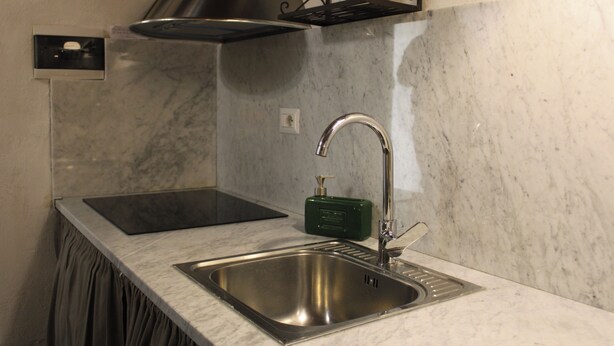 Una cocina con un lavamanos de acero inoxidable, una encimera negra, un dispensador de jabón verde y una campana extractora negra.