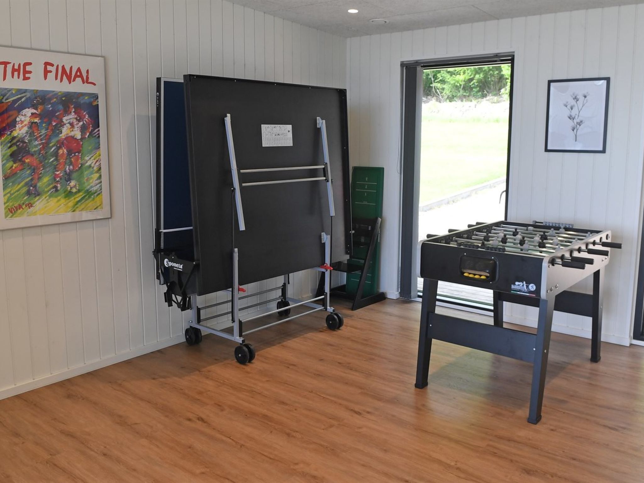 A room with a foosball table, a whiteboard, and a painting on the wall.