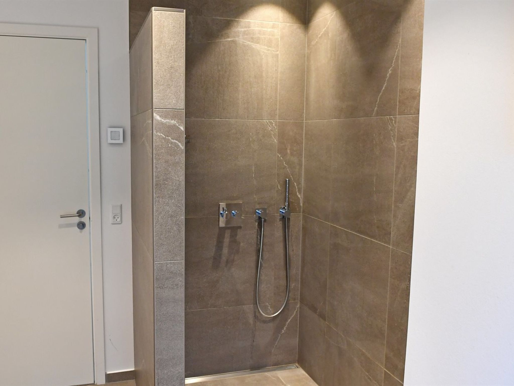 A modern bathroom with a shower, a door, and a wall-mounted light fixture.