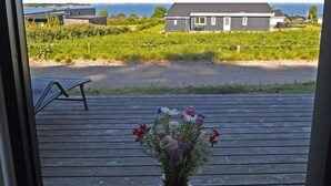 Une terrasse en bois agrémentée d’un vase de fleurs, d’un banc et offrant une vue sur les maisons et la mer.