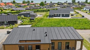 Un bâtiment moderne doté d’un toit plat, de grandes fenêtres et d’un espace extérieur couvert aménagé avec des sièges.