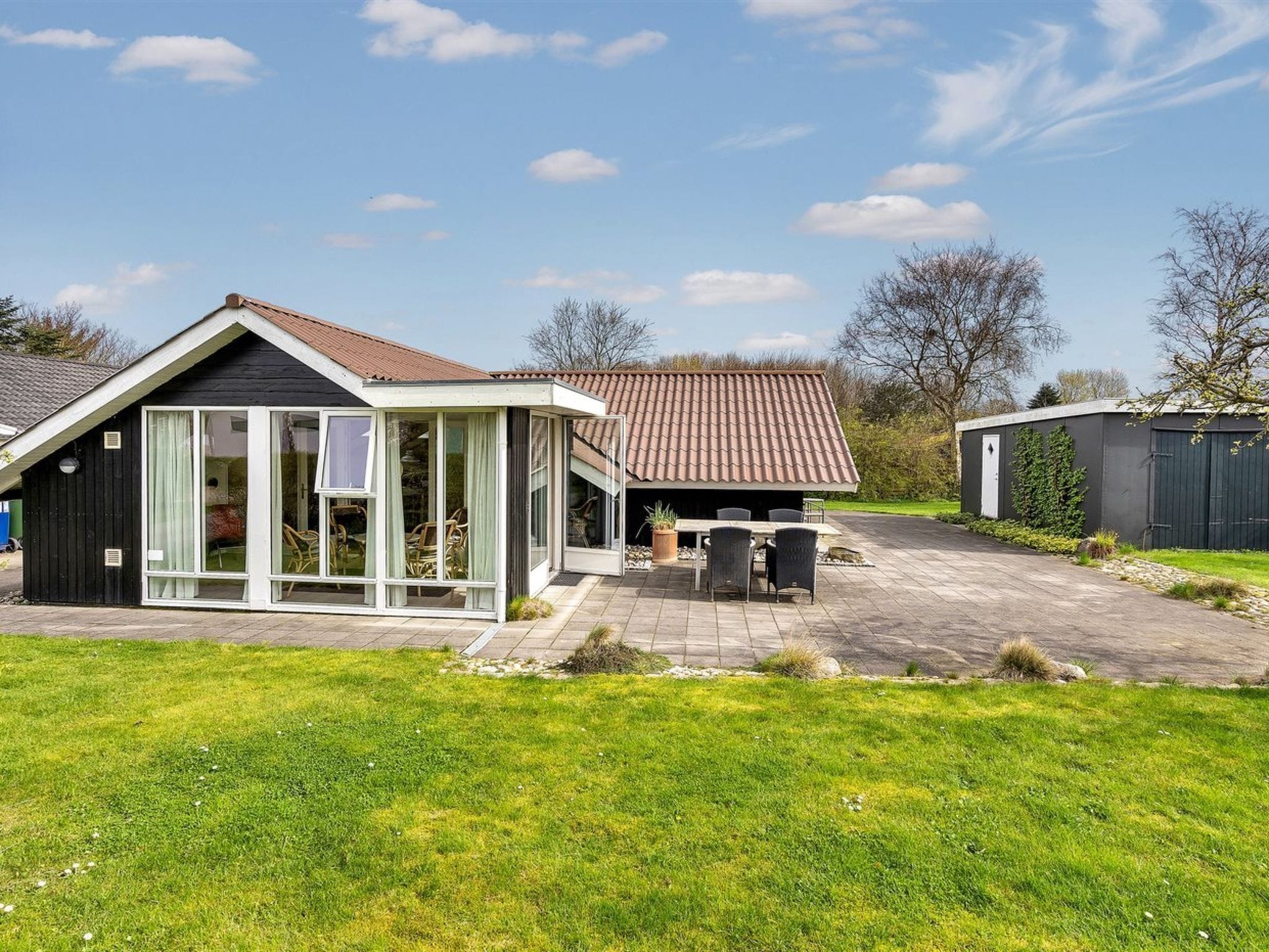 A residential property with a large glass-enclosed patio, a separate building with a tiled roof, and a well-maintained lawn.