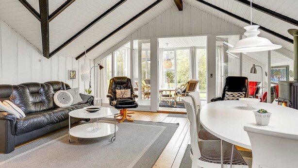 Un salon spacieux avec un plafond haut, un canapé en cuir, une table basse et un coin repas avec une table et des chaises blanches.