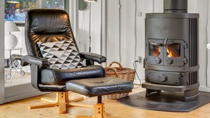 Un salon moderne avec un fauteuil en cuir, un plancher en bois, une grande fenêtre ornée d’un tableau et un poêle à bois.