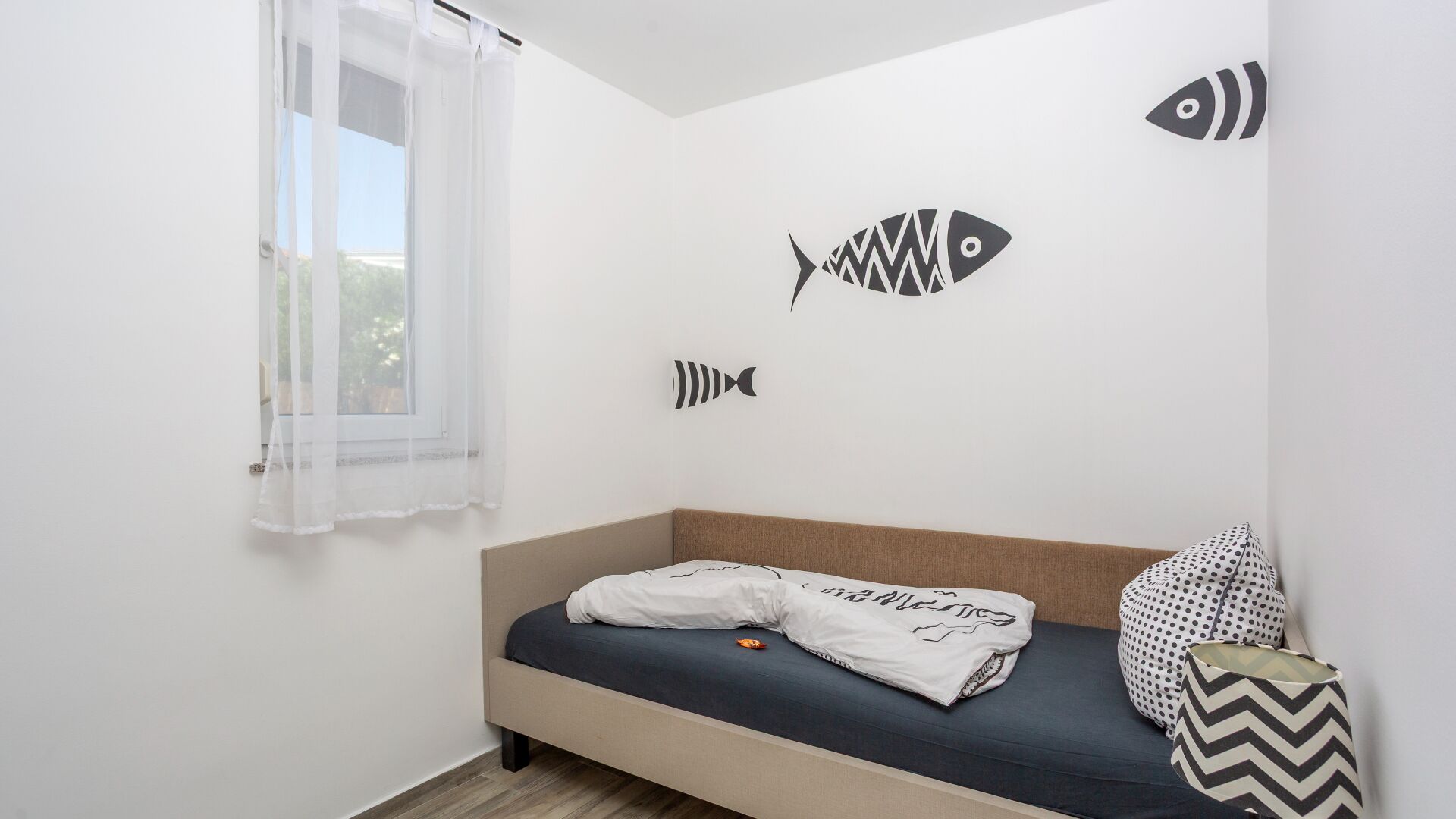 A bedroom with a bed, a window with sheer curtains, and wall art of fish.