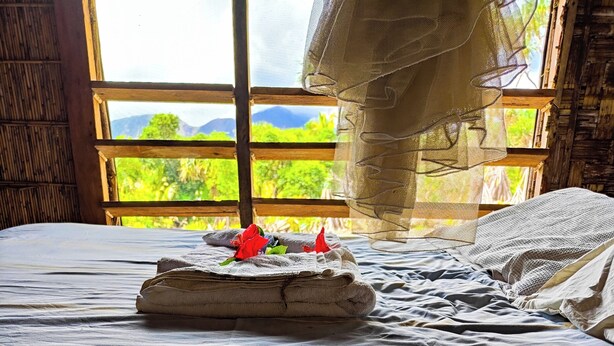 Een bed met een wit laken en een handdoek met rode bloemen.