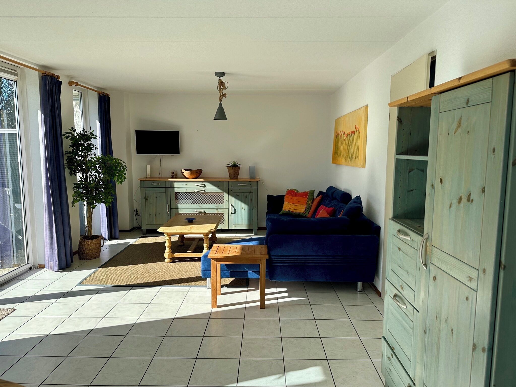 A living room with a blue sofa, a wooden coffee table, a TV on the wall, and a large cabinet.