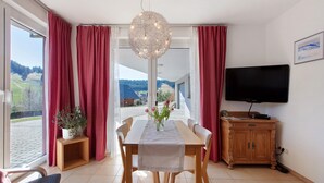 Un espace repas comprenant une table, des chaises, un lustre, un téléviseur et une vue sur l’extérieur.