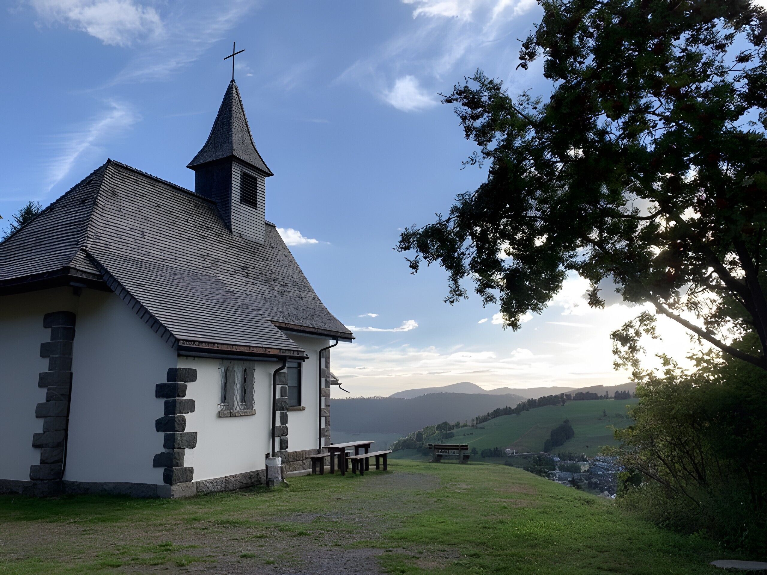 A church with a steeple, stone walls, a bench, and a picnic table.