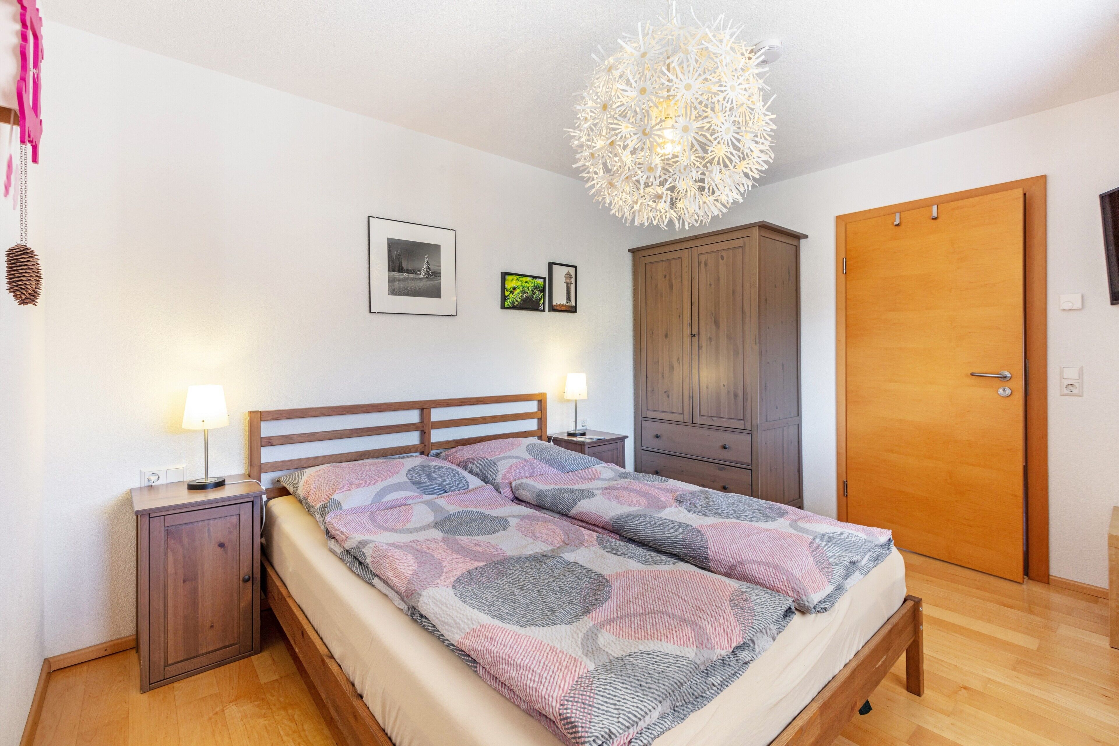 A bedroom with a bed, bedside tables, a wardrobe, a door, and a hanging light fixture.