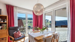 Une pièce moderne comprenant une table à manger, des chaises, un canapé et une grande fenêtre donnant sur la campagne.