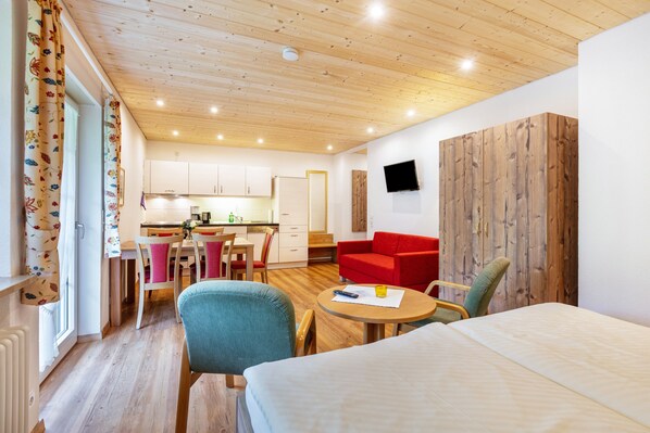 Una habitación moderna con una cama, una mesa de comedor, un sofá rojo y una zona de cocina.