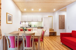 Una cocina moderna con armarios blancos, una mesa de comedor de madera con sillas y un sofá rojo.