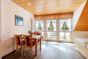 A room with a dining table, chairs, a bed, and large windows with curtains. - Apartment 'Stübenwasen' with Balcony and Wi-Fi (Todtnau)