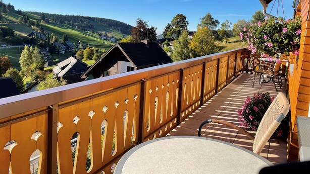Un balcon donnant sur une vallée verdoyante, avec une balustrade en bois et des meubles d’extérieur.