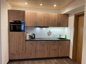 A modern kitchen with wooden cabinets, a built-in oven, a coffee maker, and a sink. - Apartment 'Ferienwohnung Belchen' with Balcony and Wi-Fi (Todtnau)