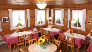 Une cabane en bois dotée de plusieurs tables à manger, chacune recouverte d’une nappe rose et entourée de chaises en bois.