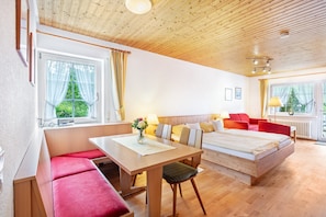 Une pièce avec un plafond en bois, un lit, un bureau avec une chaise, un banc et une fenêtre avec des rideaux.