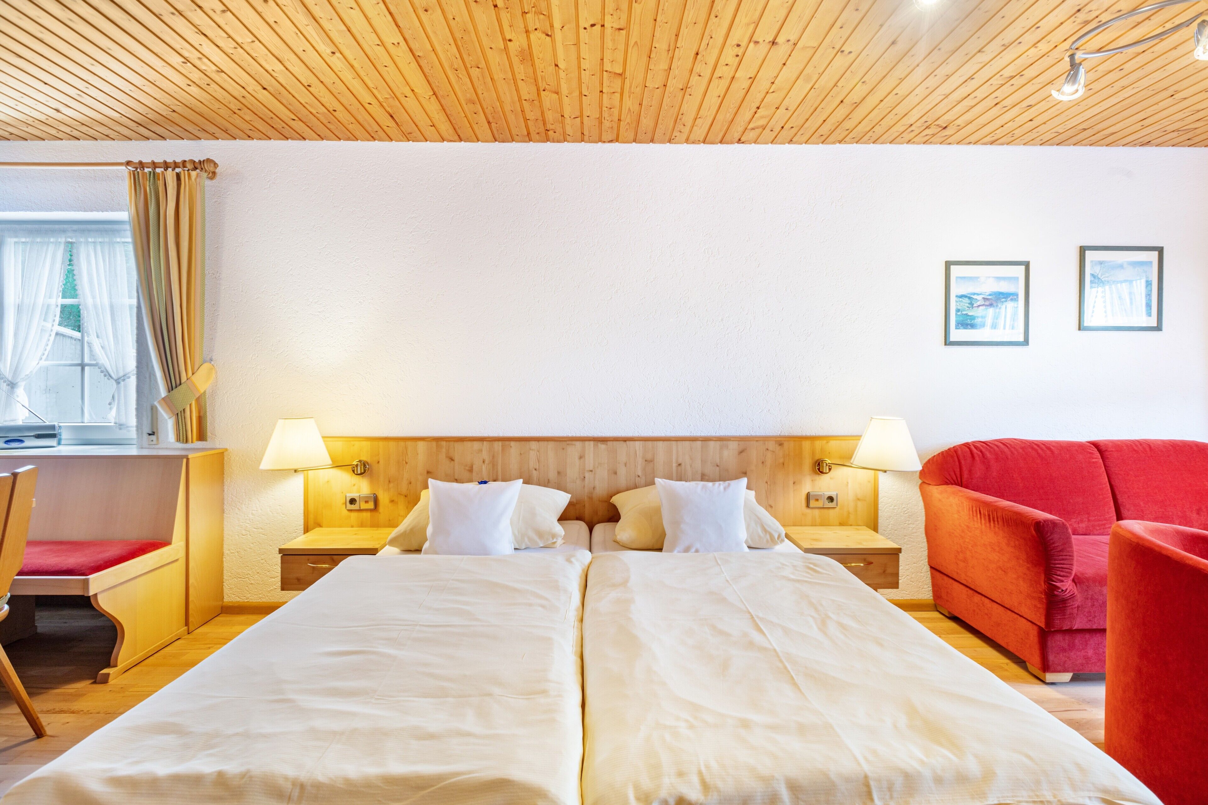 Un lit double avec deux tables de chevet, un canapé rouge et une fenêtre avec des rideaux.