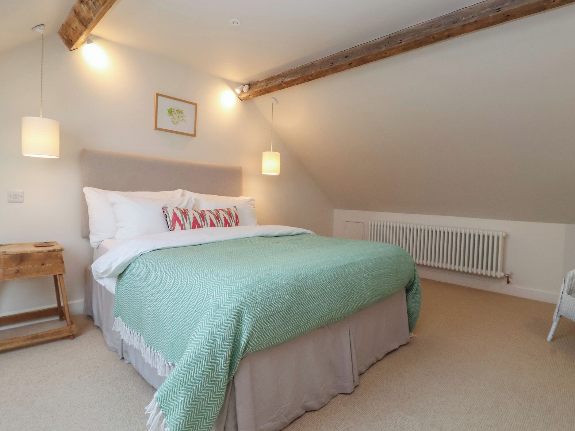 A bedroom with a bed, a nightstand, a wooden headboard, a radiator, and a picture on the wall.