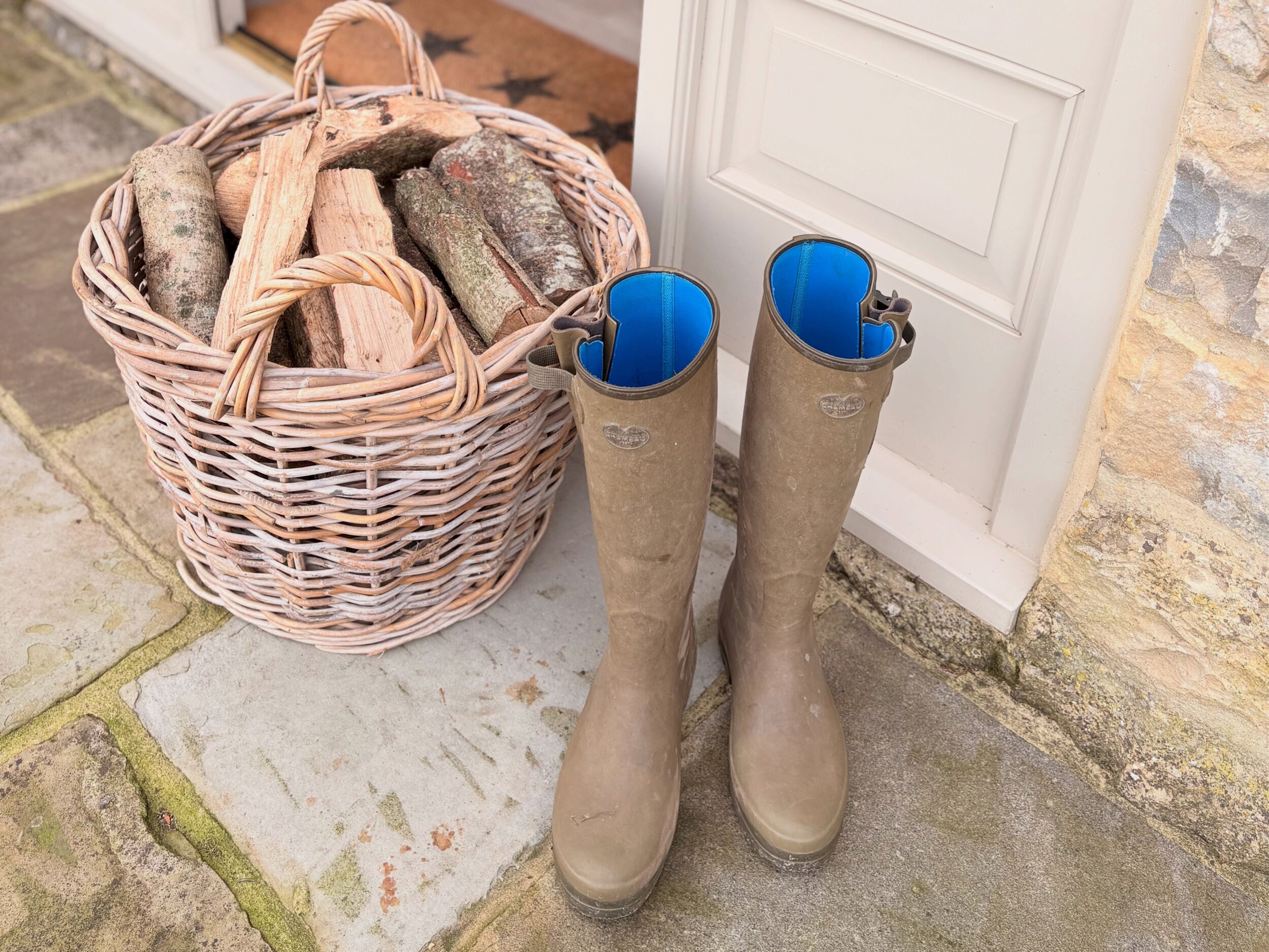 A wicker basket filled with logs and a pair of brown boots with blue interiors.