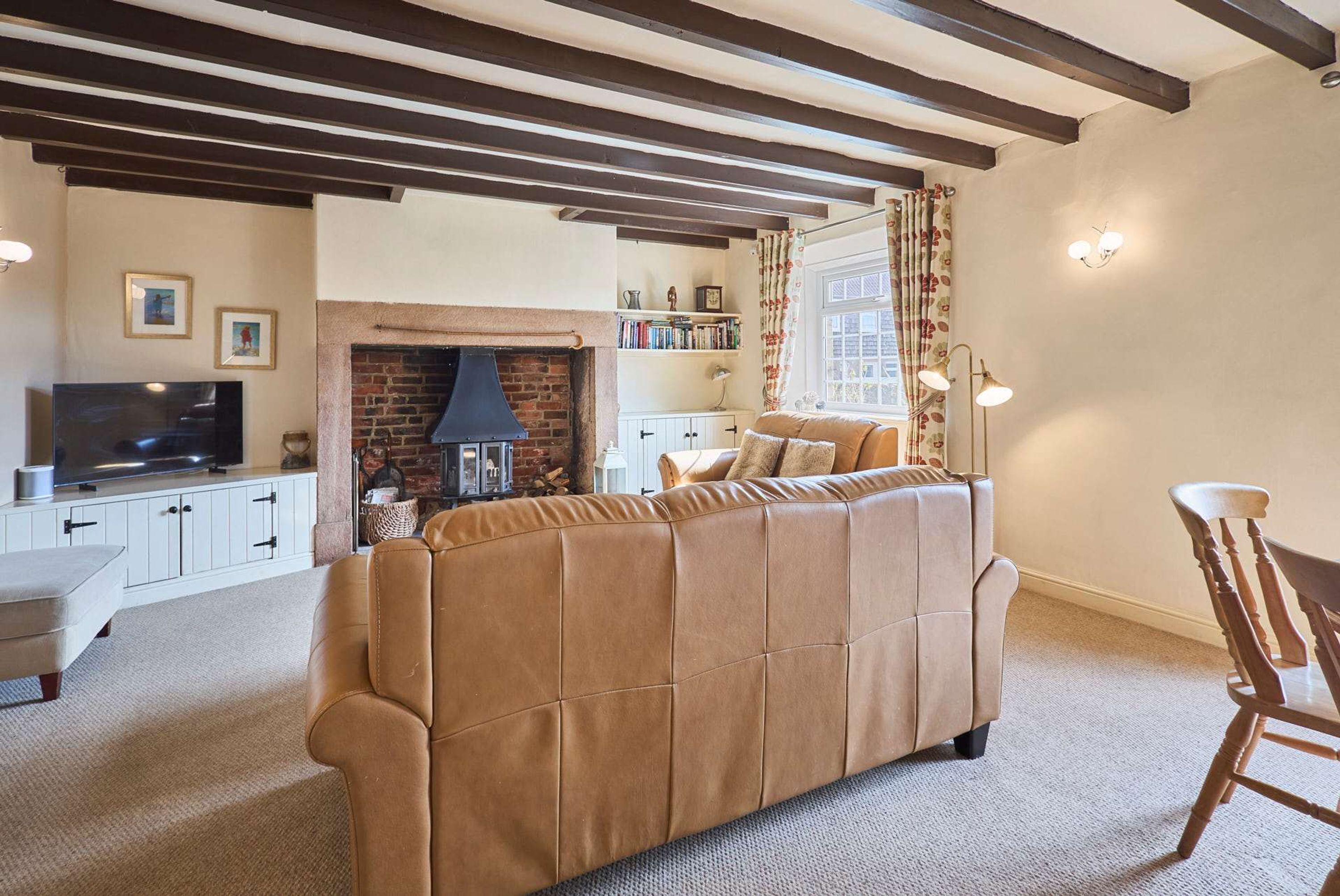 A living room with a brown sofa, a television, a fireplace, and a bookshelf.