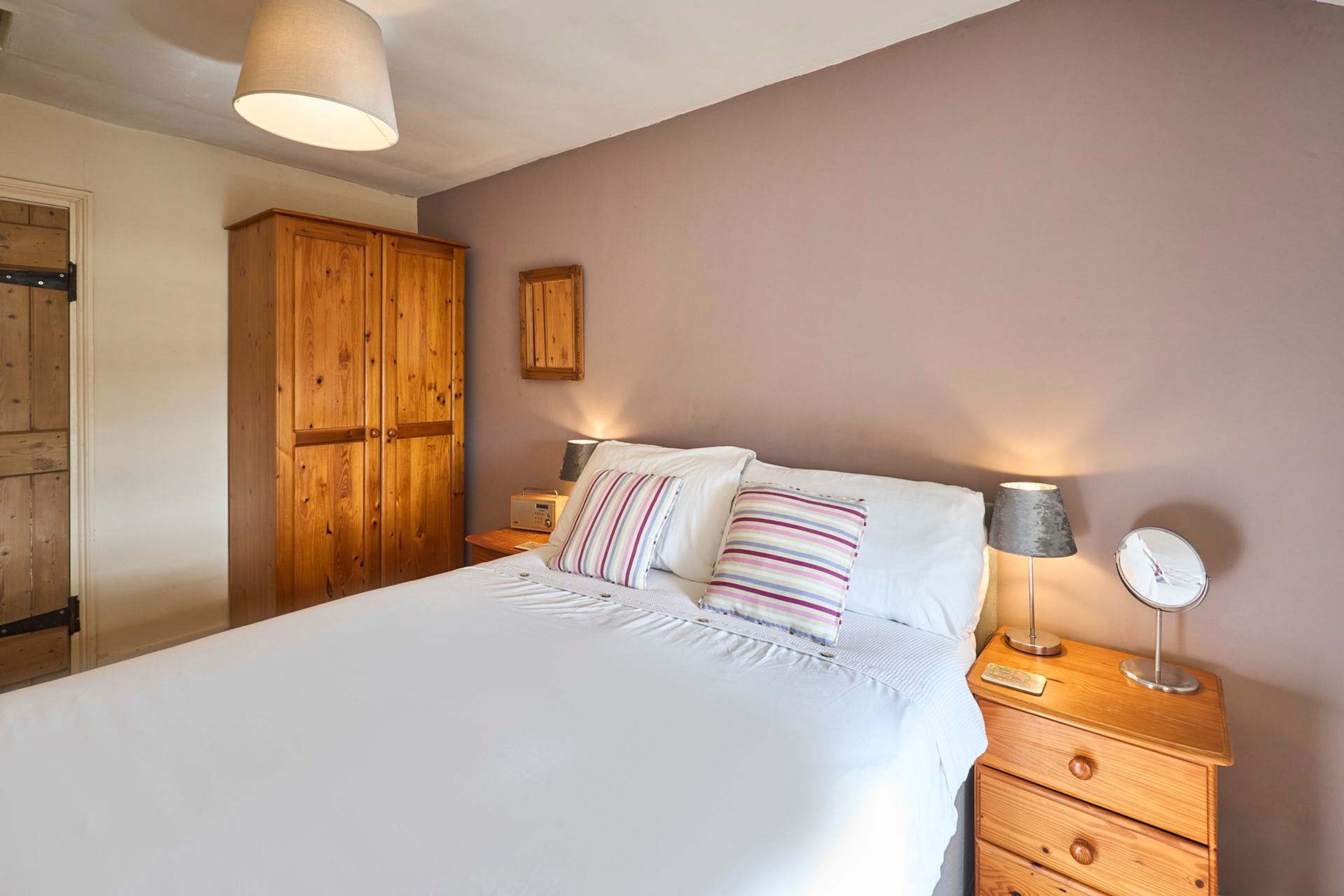 A bedroom with a large bed, wooden wardrobe, bedside tables with lamps, and a small mirror.