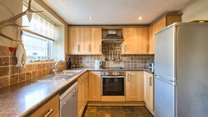 Een keuken met houten kastjes, een roestvrijstalen koelkast en een betegelde spatwand.