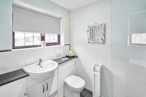 Un baño con lavamanos, inodoro y ventana con persianas.