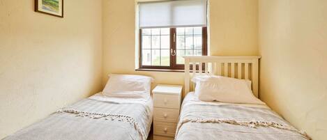 A small, cozy bedroom with two single beds, a nightstand, a window with a view, and a framed picture on the wall.