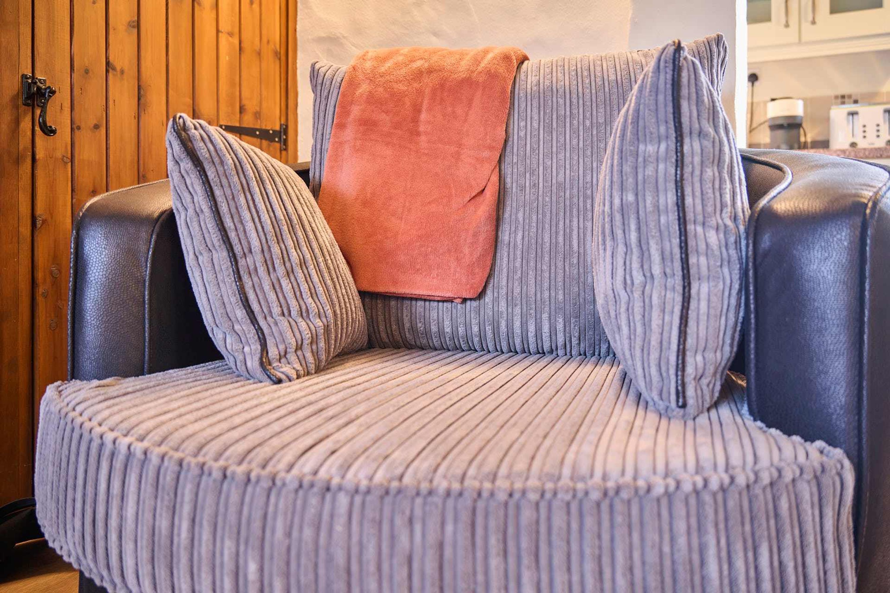 En lædersofa med et rillet mønster og et orange pled.