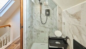 Une salle de bain moderne avec une douche en verre, des carreaux de marbre, un lavabo noir avec un miroir et un escalier en bois.