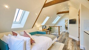 Une chambre avec un plafond en pente, des fenêtres de toit, un lit avec des oreillers, un bureau et un téléviseur.