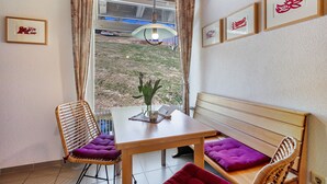 A room with a wooden table, two wicker chairs with purple cushions, a bench with a wooden backrest, and a window with curtains. - Apartment Hedi, 35 sqm with Mountain View, Balcony and Wi-Fi (Todtnau)