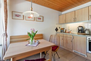 A kitchen with wooden cabinets, a dining table with a vase of flowers, and a hanging light fixture.