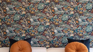 Een bank met twee oranje kussens tegen een muur met een bloemenprint.