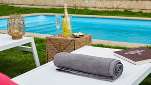 Een zwembadterras met een rieten tafel, een opgerolde handdoek, een boek en twee champagneglazen.