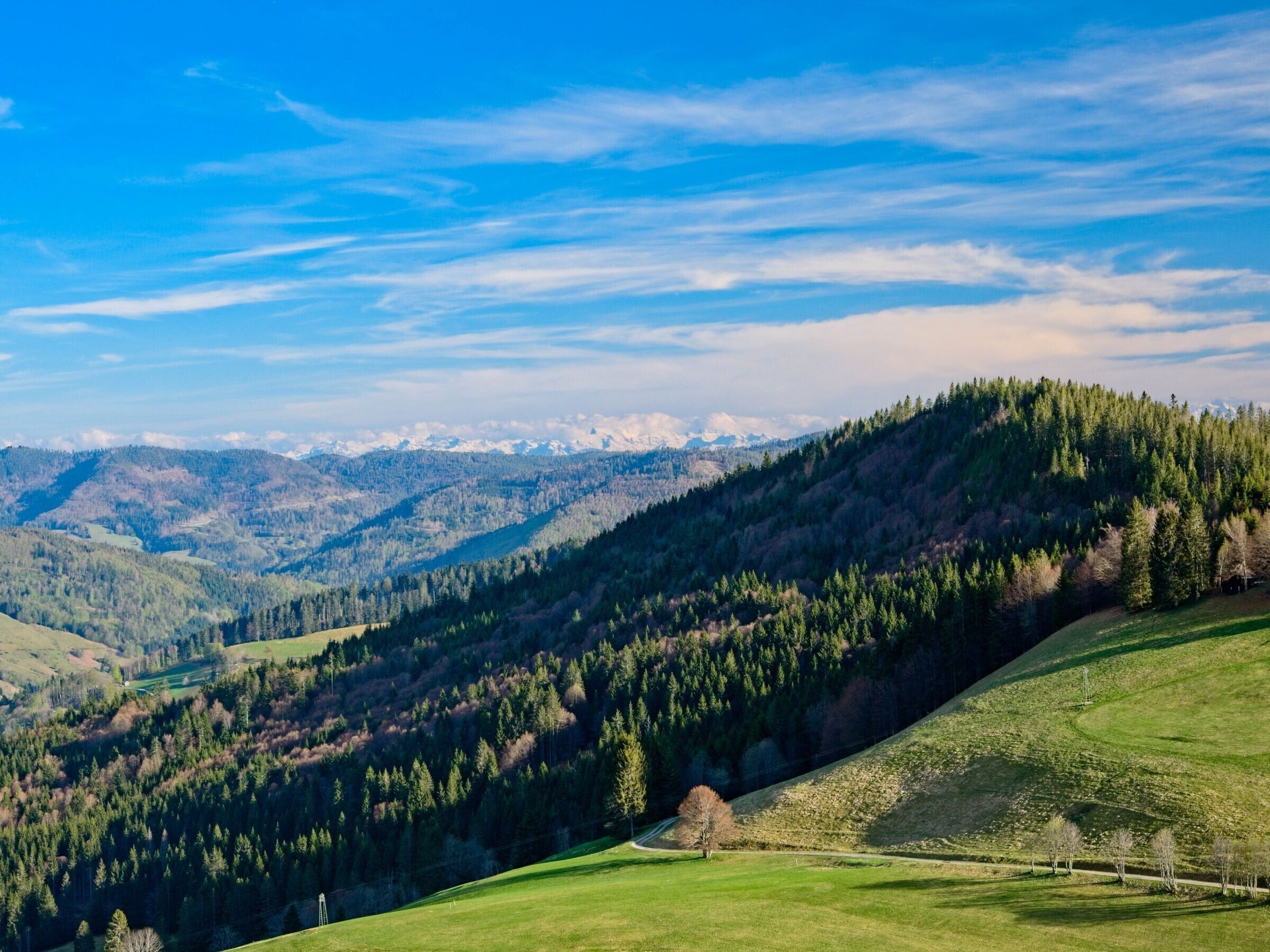 A mountainous landscape with a clear sky, a winding road, and a small building on a hill.