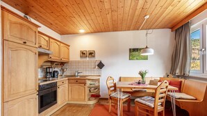 A kitchen with wooden cabinets, a stove, and a dining area with a table and chairs. - Apartment Eddy, 45 sqm with Mountain View, Meadow and Wi-Fi (Todtnau)