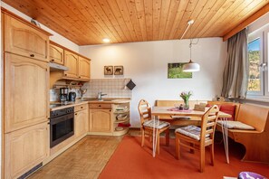 A kitchen with wooden cabinets, a stove, and a dining area with a table and chairs. - Apartment Eddy, 45 sqm with Mountain View, Meadow and Wi-Fi (Todtnau)