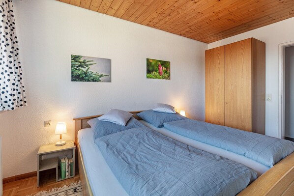 Une chambre avec deux lits, une table de chevet avec une lampe et deux tableaux encadrés au mur.