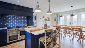 A modern kitchen with a star-patterned backsplash, stainless steel appliances, and a central island with bar stools. - Host Stay Kittiwake Cottage (Bridlington)