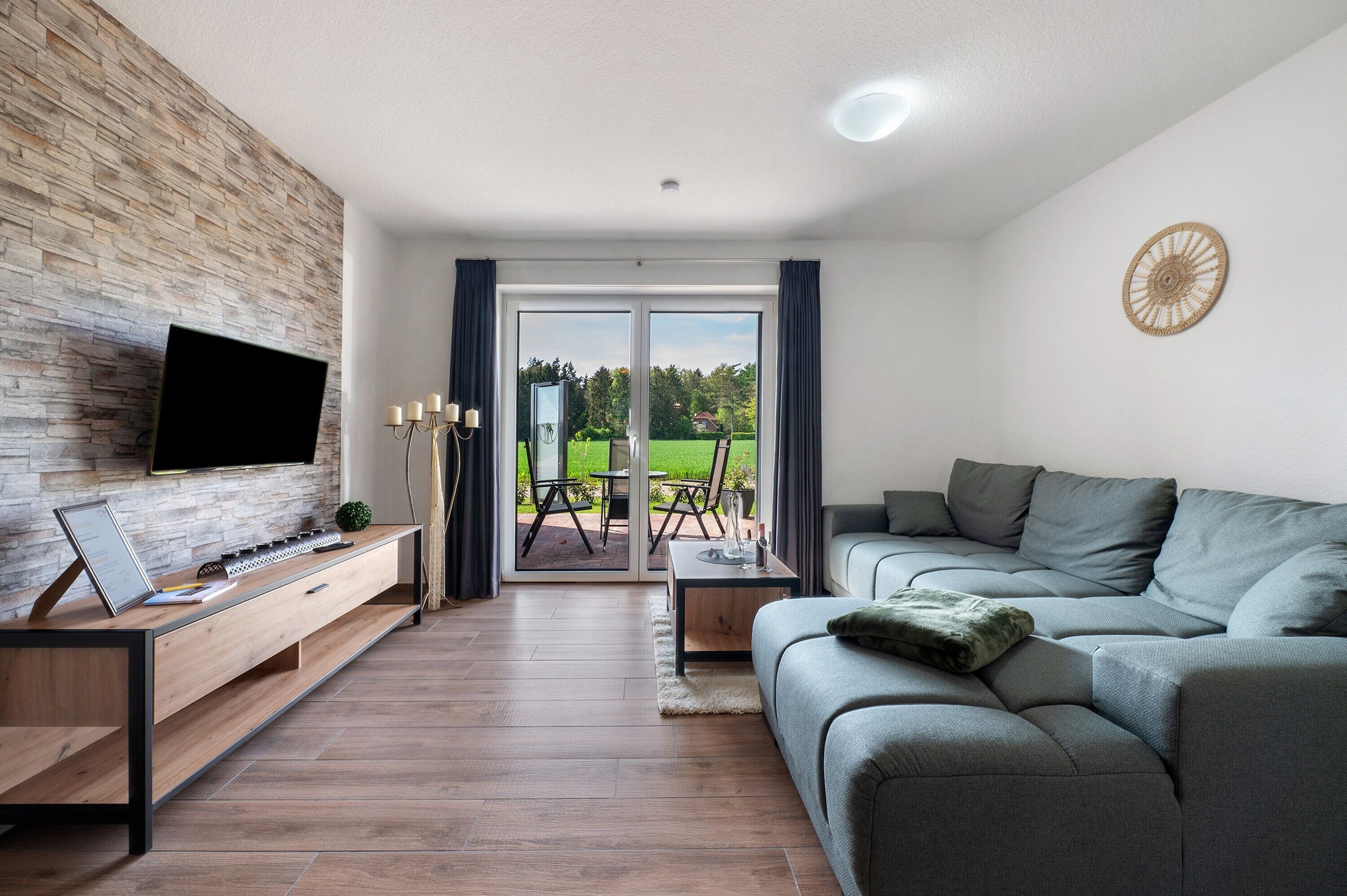 Una sala moderna con televisor de pantalla plana, consola de madera, sofá gris y vistas a un patio exterior a través de puertas de cristal.