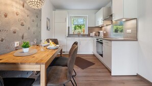 A modern kitchen with white cabinets, a wooden dining table, and a hanging light fixture. - Holiday Apartment 'Anna 1 Eg' with Private Terrace and Garden (Suhle)