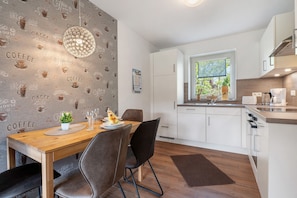 Une cuisine moderne avec des meubles blancs, une table à manger en bois et un mur décoré sur le thème du café.